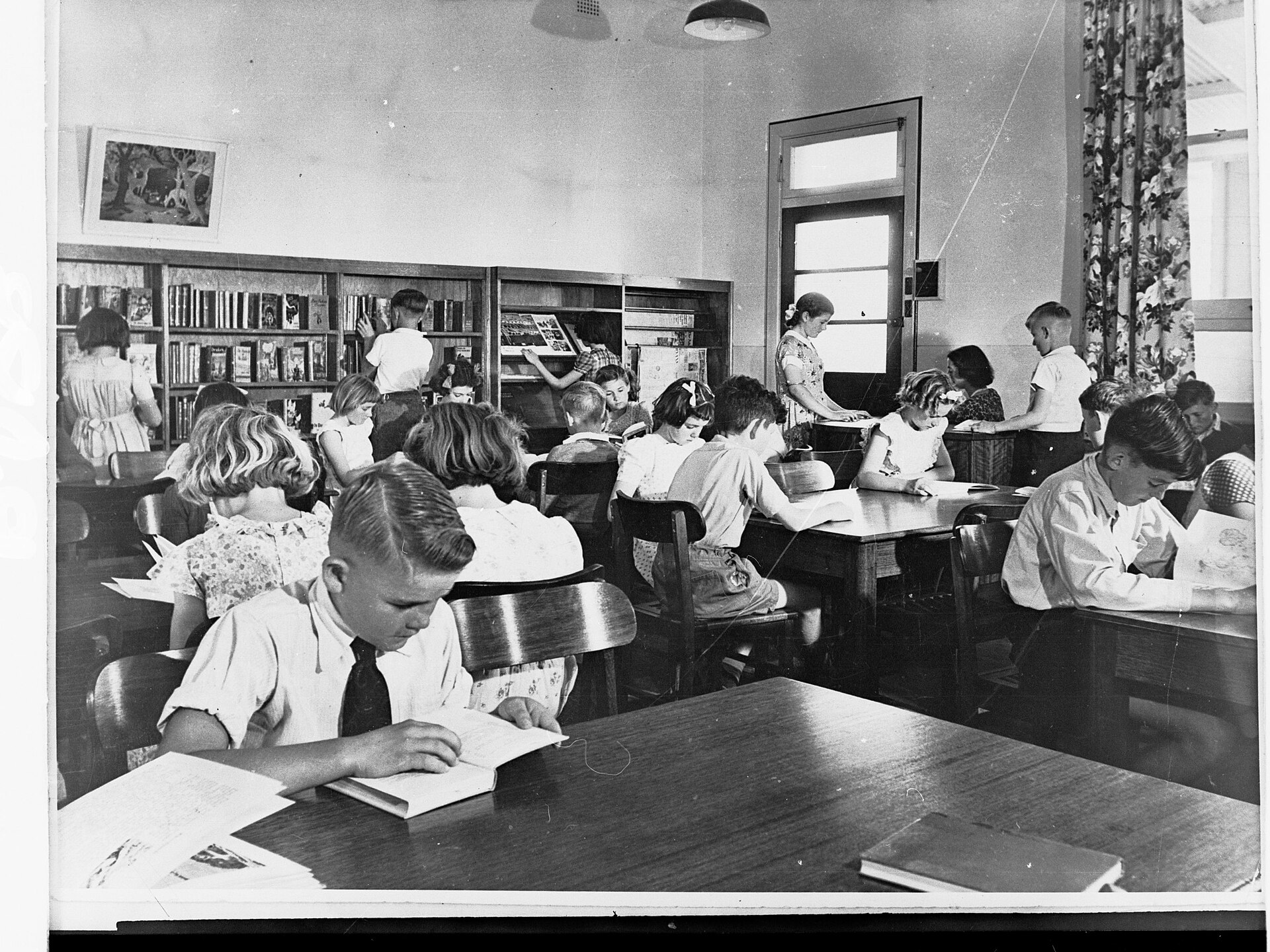 Dzieci czytające przy stołach w bibliotece szkolnej — obraz popołudnia, które rozwija zamiast przechowywać.